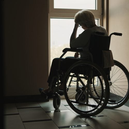Lonely,Senior,Woman,Looking,Through,The,Window,Of,The,Nursing